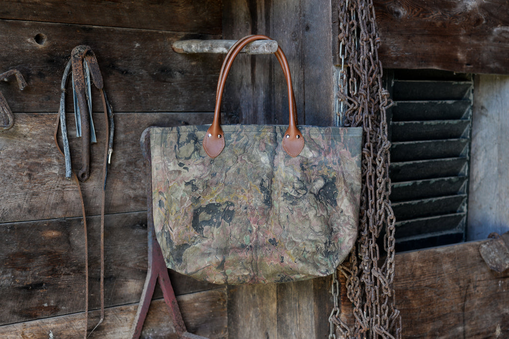 Vintage-style leather bag with camouflage pattern hanging on a wooden wall.