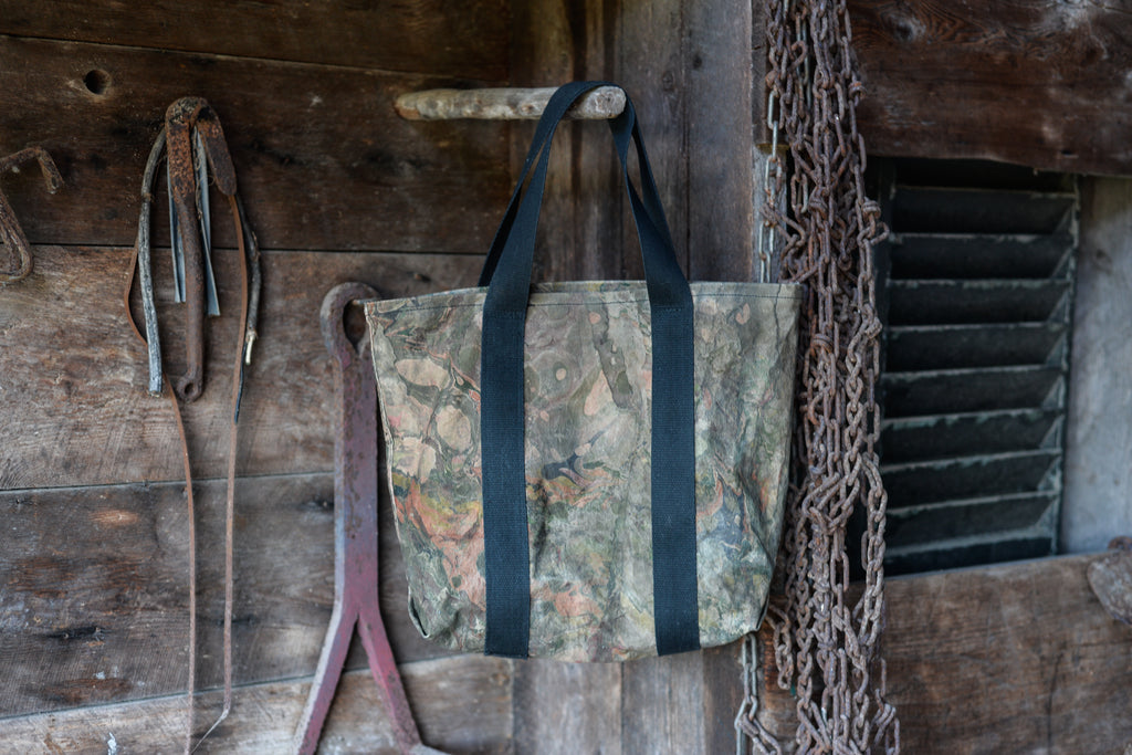 Camouflage bag with black straps hanging on a wooden wall with tools and chains.